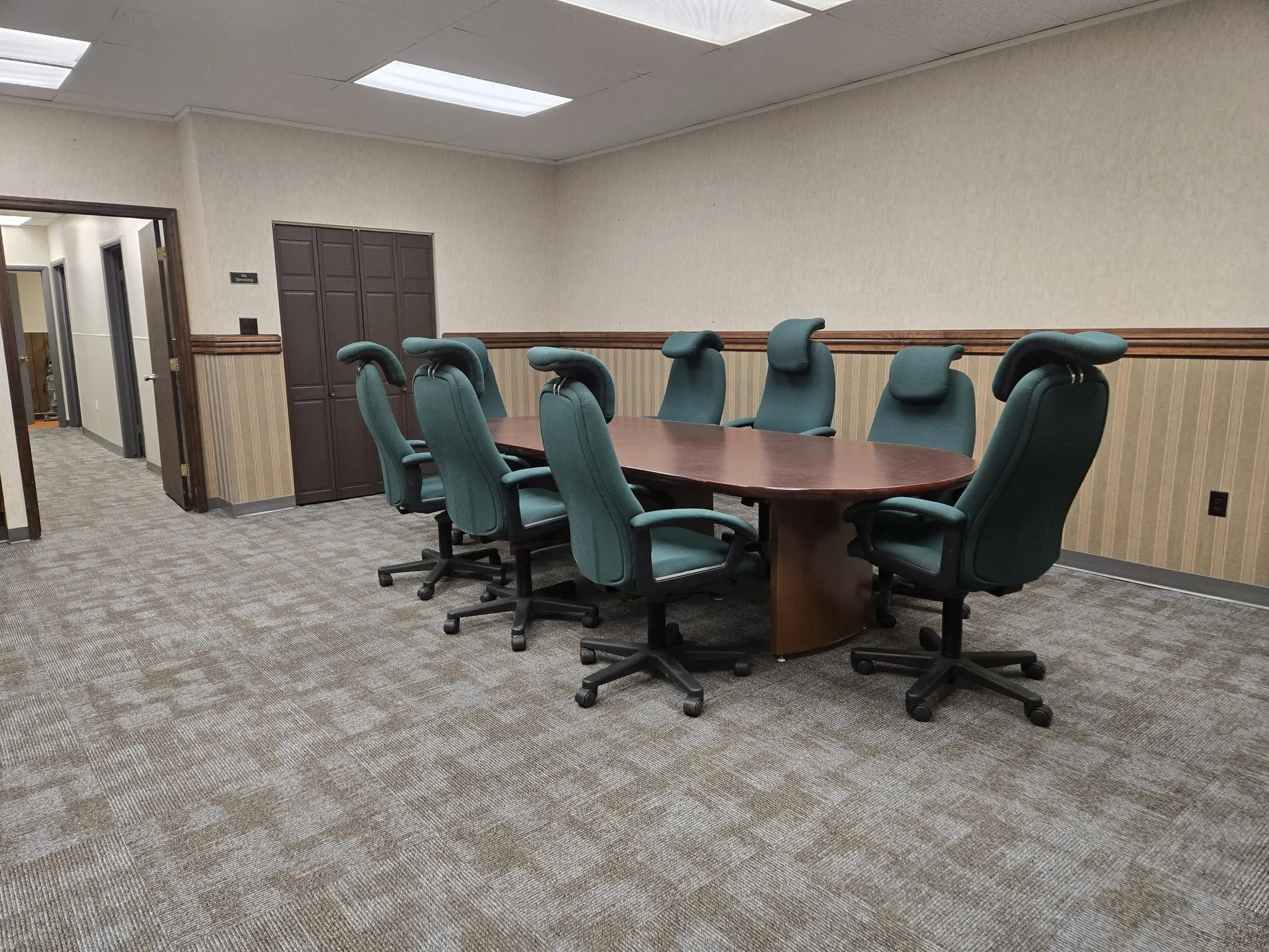 Conference room with a large wooden table and green office chairs